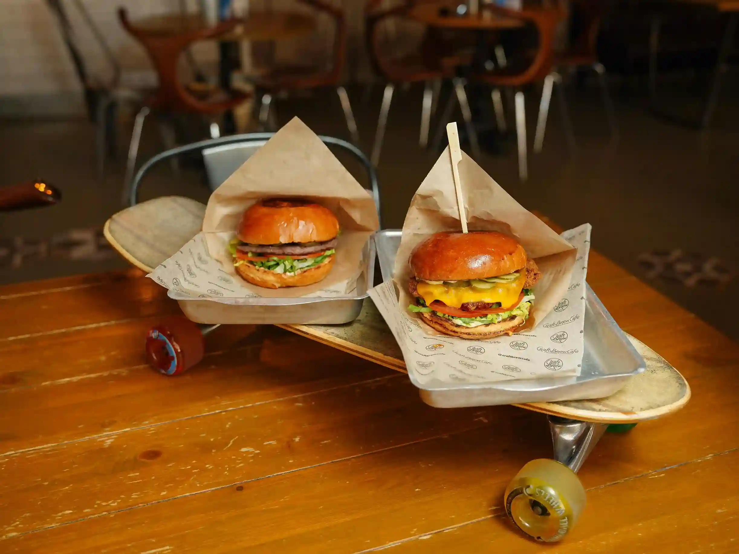 Two burgers in food trays wrapped in custom printed food paper, placed on a skateboard on a table, showcasing an eco-friendly presentation with a unique style